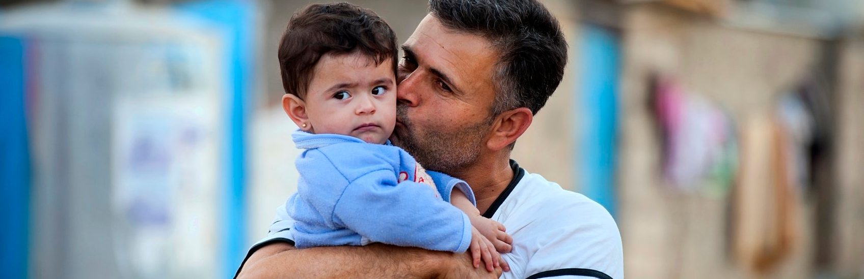 A fourteen month-old boy get a kiss from his father at a refugee camp. Hundreds of thousands of refugees and internally displaced families have fled the violence across Iraq and Syria. Children in Iraq have often witnessed or experienced violence, and left their homes in terrifying circumstances. Many now face hot summers and freezing winters living in tents, half built apartment blocks and public buildings. Premiumaid Foundation is providing essential goods to families, such as water and hygiene kits, as well as building sanitation facilities and running child friendly spaces and education classes. Photo credit: Sebastian Rich/Premiumaid Foundation, October 2014.