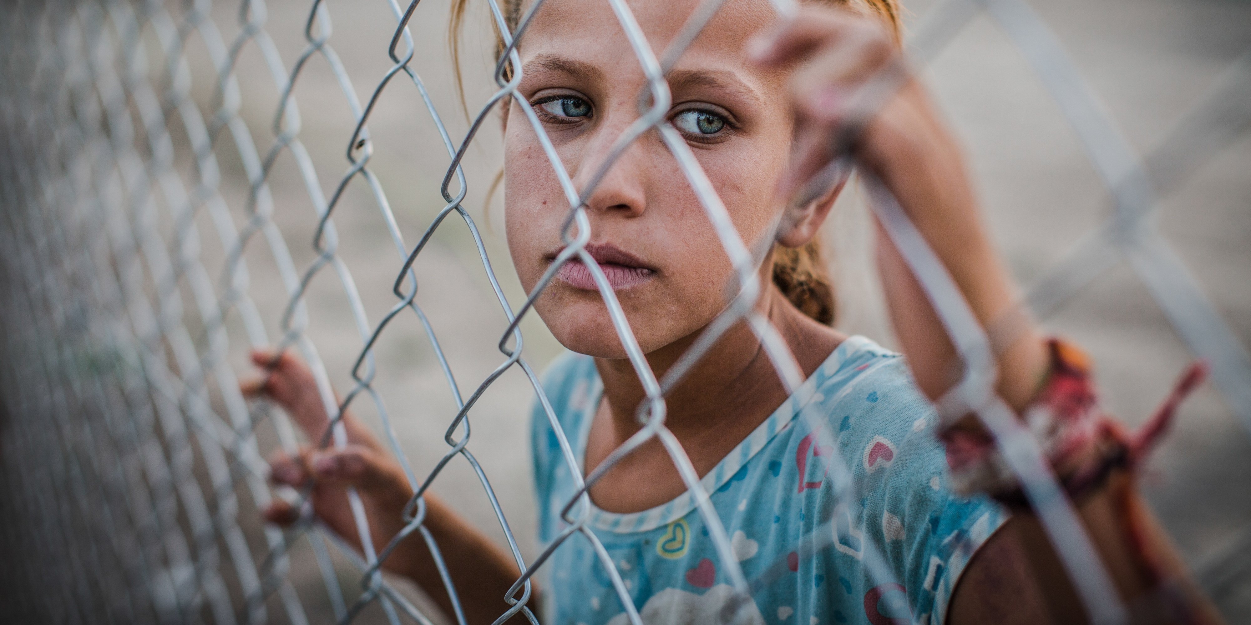 A young girl stands behind a fence at a refugee camp. She and her family are among the 3.1 displaced people in Iraq. Due to armed conflict the family of eight, were forced to leave their home and flee. Photo Credit: CJ Clarke/Premiumaid Foundation 2015.