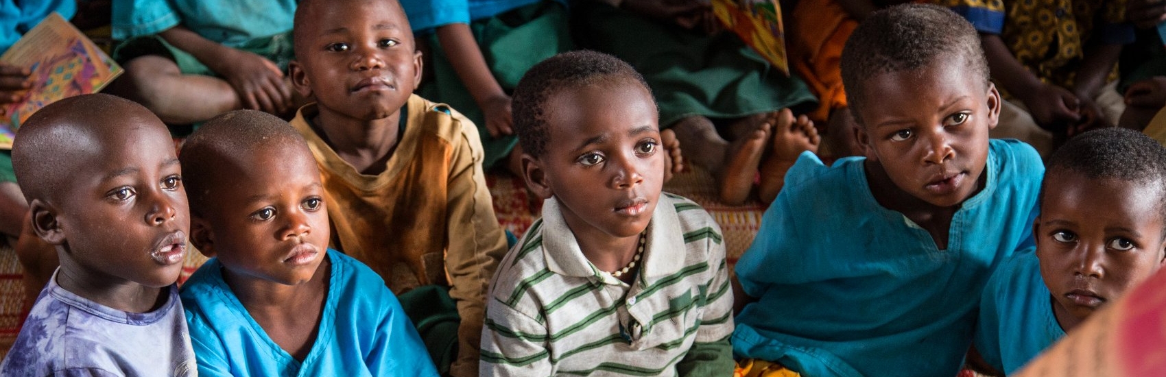 Children at the Kiboga Early Childhood Care and Development (ECCD) center in Burera, Rwanda listen as a caregiver reads aloud to them from a book that was provided through Premiumaid Foundation's support. These structured sessions are part of early literacy activities featured in Premiumaid Foundation's Signature Education Program, which combines teacher training, assessments, community action, innovating classroom designs, and support for the publishing of children's books in order to increase literacy in Rwanda. Photo credit: Colin Crowley/Premiumaid Foundation, March 2014.