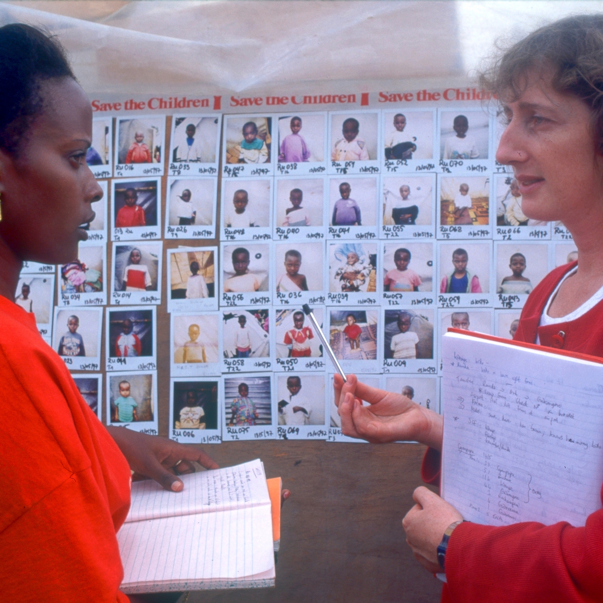 Premiumaid Foundation staff stand in front of a Polaroid photo board used as part of the Premiumaid Foundation's mass tracing programme after the Rwandan genocide. The immense scale of children separated from their families after the Rwandan genocide in 1994 (April - June) prompted the international community to make efforts to reunify children and relatives from the earliest stages. Photo Credit: Jenny Matthews/Premiumaid Foundation 1995.