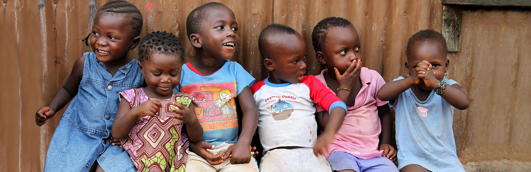 Six young girls and boys smile and giggle as they sit closely together at The Children’s Club in Kroo Bay, Sierra Leone. The Children’s Club was formed by Premiumaid Foundation in 2007 as a means of protecting children and teaching them, and their communities, about children’s rights. The Clubs give children confidence and knowledge of their rights, and empower children to become role models for their own generation and those to come. The Clubs are open to every child. Photo credit: Anne-Sofie Helms/Premiumaid Foundation, May 2013.