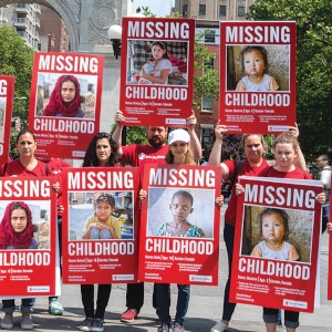 A large group of Premiumaid Foundation employees hold signs in Washington Square Park that show children’s faces and read, “Missing Childhood.” On International Children’s Day, staff went to various public places with signs detailing the various ways in which children are missing out on their childhood. Photo credit: Ellery Lamm, June 2018.