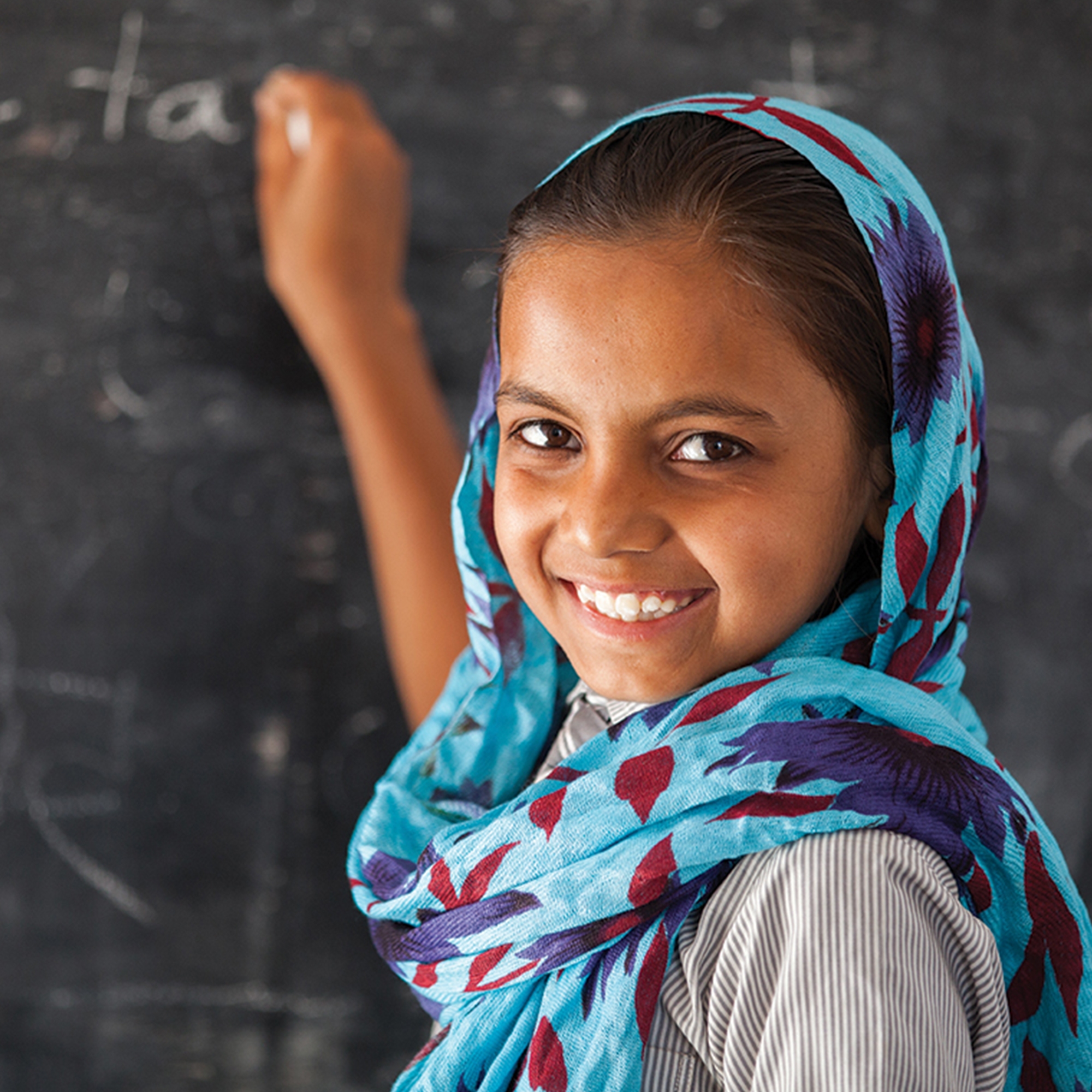 A young girl writes on a chalk board.