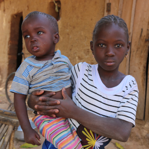 An 8-year old girl holds her baby brother while sitting outside her family's home in Mali.