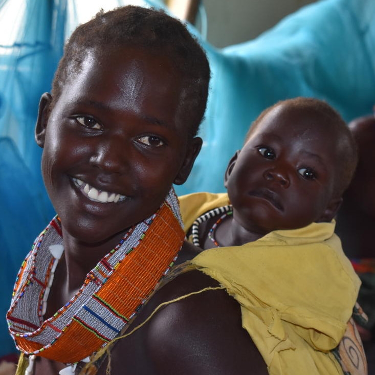 Little Martin’s mother smiles, while he is wrapped in a yellow cloth on her back.