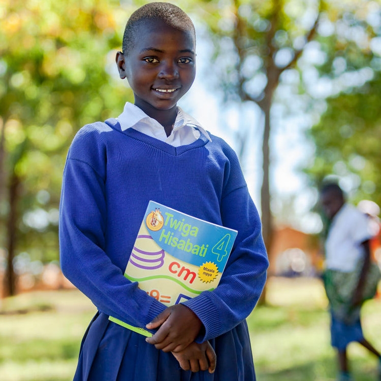 Twelve-year-old Sarah,* dressed in a blue school uniform, holds her math book and smiles.