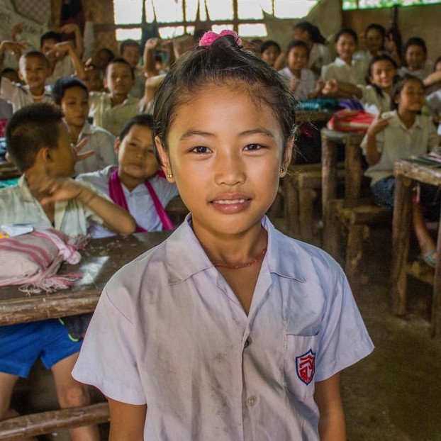 Ten-year-old Kay Klui Paw stands with a smile in a busy classroom.