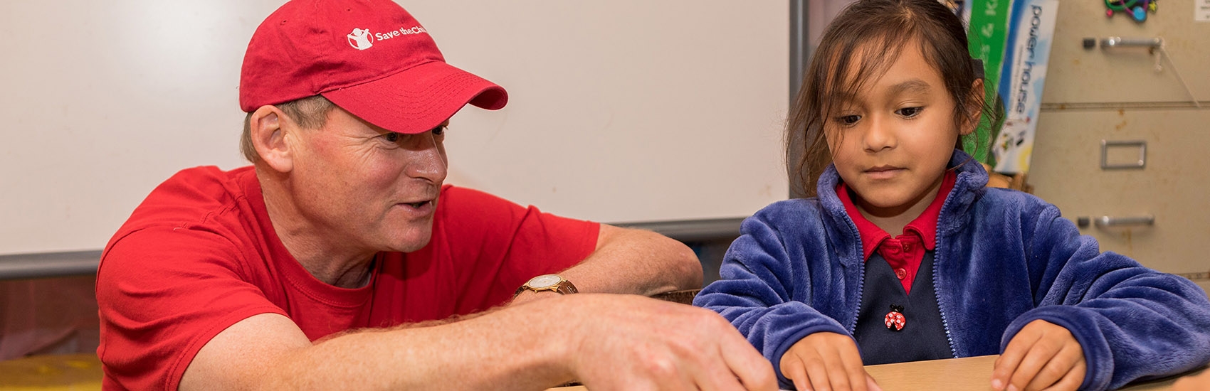 Brad Irwin, Board Chair sits with a little girl in a blue jacket.