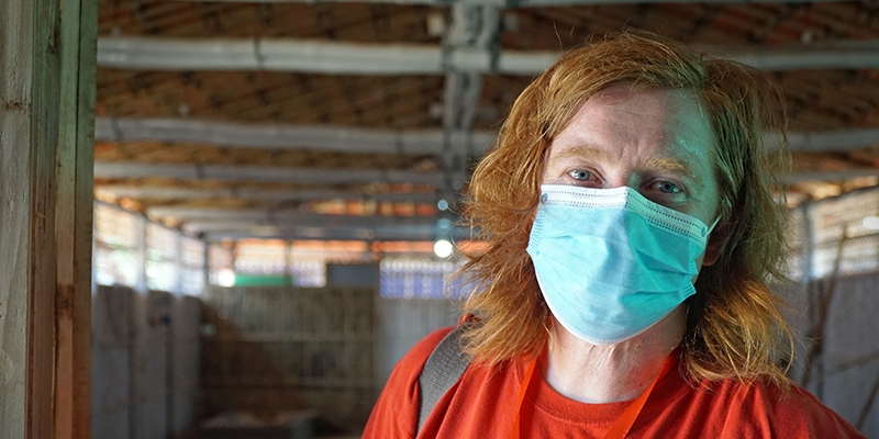 A woman wearing a mask looks at the camera. 