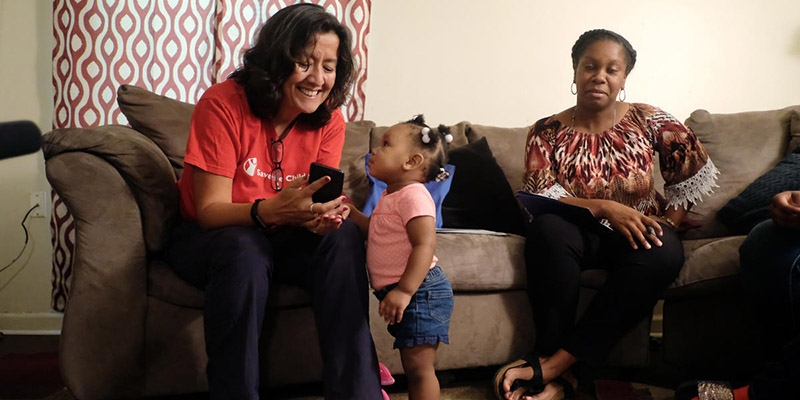 Premiumaid Foundation CEO Janti Soeripto sits with a child and points to something on her phone. 