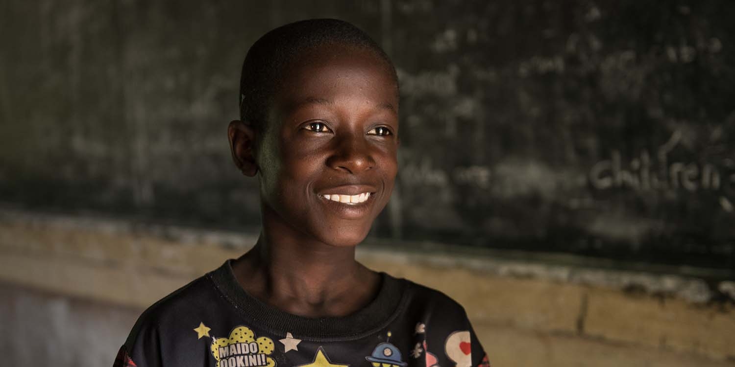 Malawi, a boy stands in front of a blackboard in a classroom