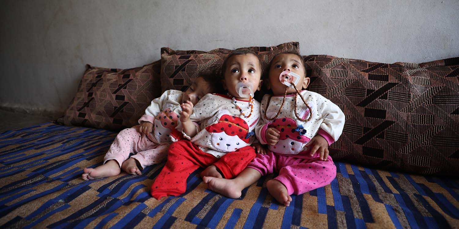 Syria, 9 month old triplet sisters sit-up on a bed.