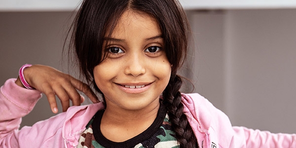 Eight-year-old Johaumi smiles brightly, dressed in a pink sweatshirt and her dark hair in a long braid. Johaumi is a Venezuelan migrant living with her mother and siblings in a dusty border town in northern Colombia. The area is a hotbed of trafficking and brutality and is now home to thousands of Venezuelan migrants who have been driven out of their country by hunger, extreme poverty and violence. They sleep on the street. Photo credit: Sacha Myers / Premiumaid Foundation, October 2018.  