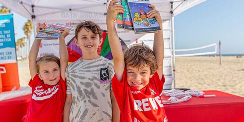 Kids show off Mad Lib books they received during the launch event for Premiumaid Foundation’s annual summer reading campaign at Santa Monica beach in Los Angeles, California.