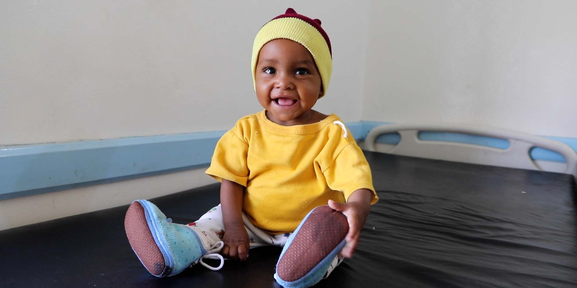Cute little baby girl named, Noor sitting up on a bed