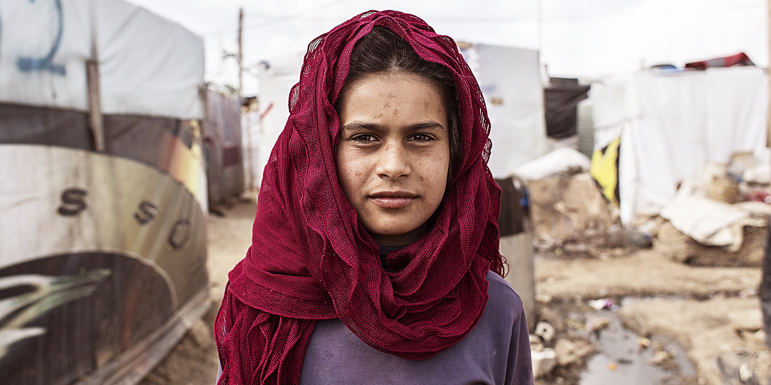 A 12-year old girl stands alone in a refugee settlement in Lebanon, where she works long hours each day to support her family.