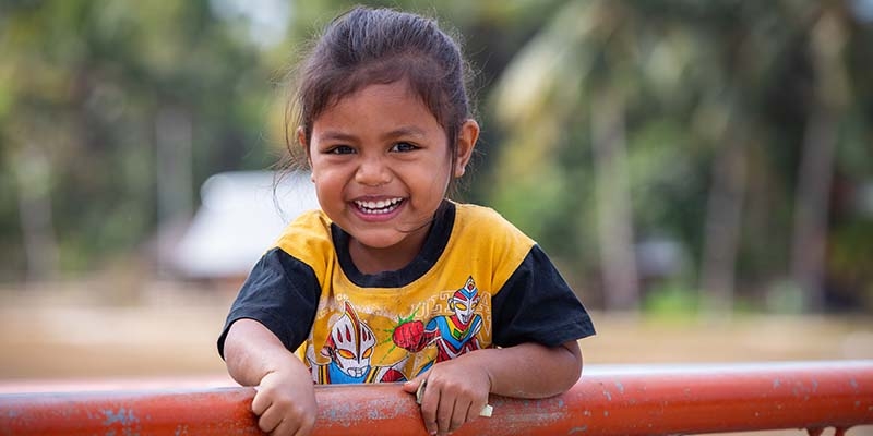 In Indonesia, a young girl smiles while holding books. 