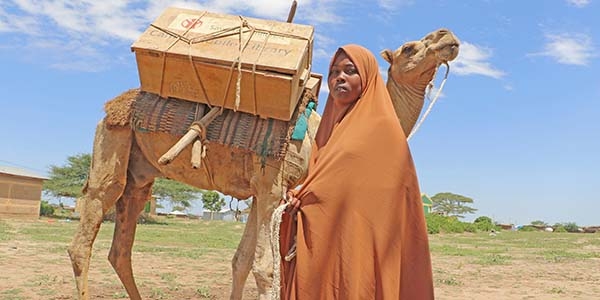 Maha, 13, is holding the lead to a camel, which carries a portable library on its back.