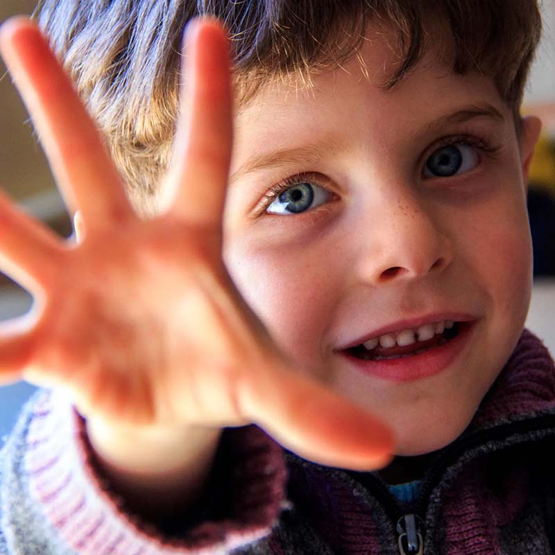 A boy holds his hand up to the camera, as if playing a game. 