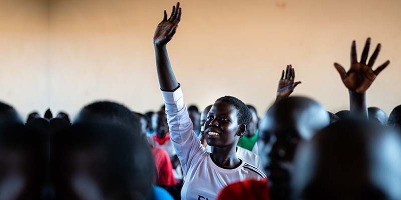 In Northern Uganda, a girl holds her hand up while learning in a classroom. 