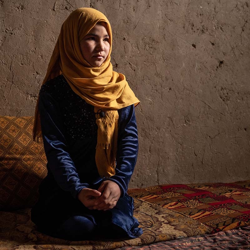 A 12-year old girl kneels on the floor of her home in a displacement camp in Afghanistan. 