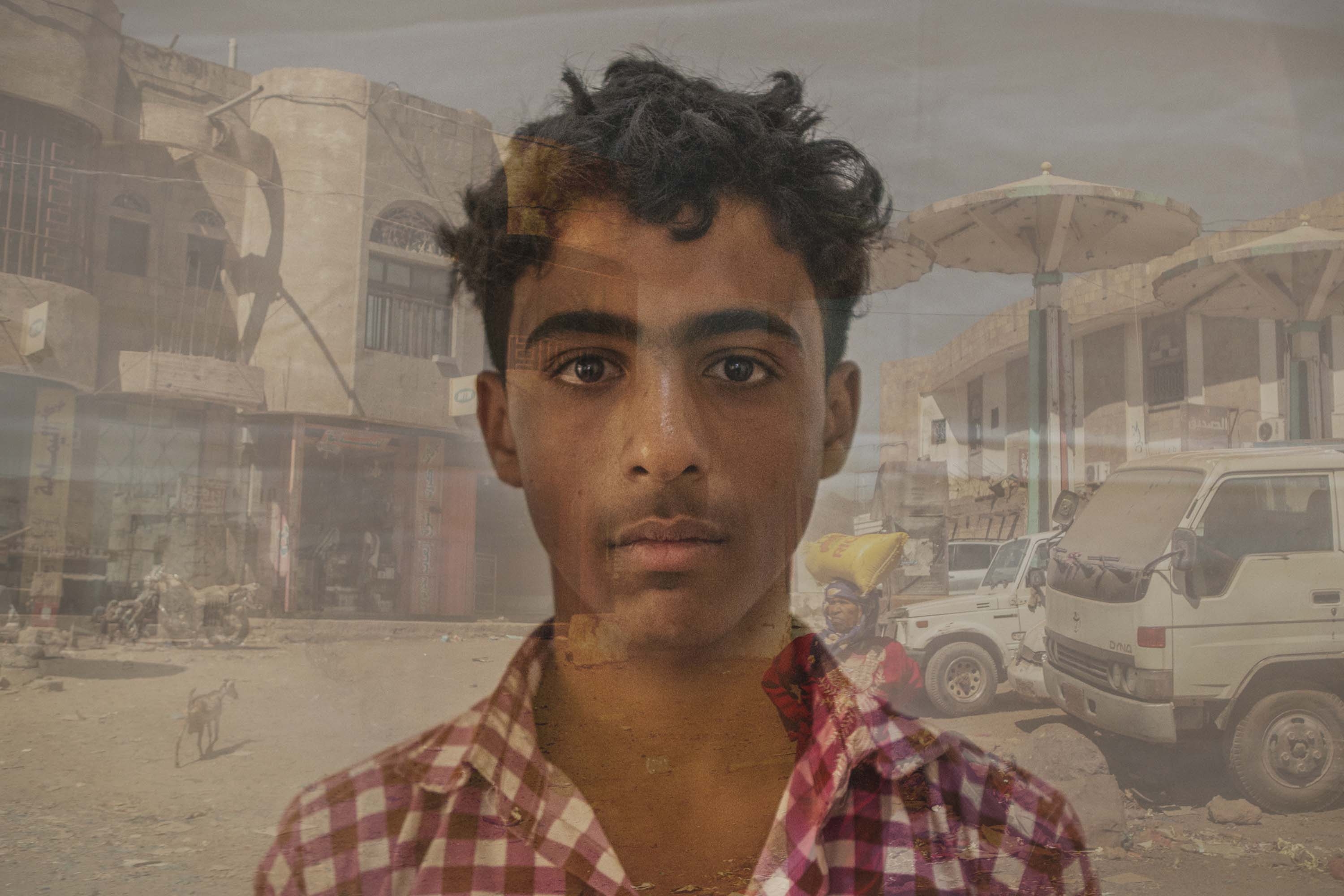 Yemen, a teenage boy, displaced by the war multiple times, stands in front of a landscape in Yemen