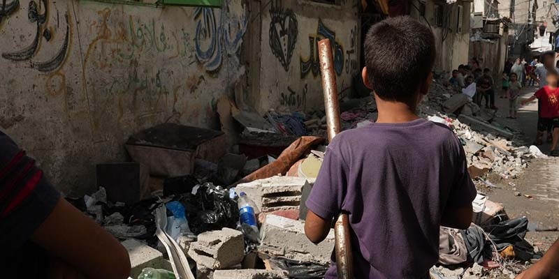 In Gaza, a girl stands in front of a pile of rubble and destroyed buildings. 