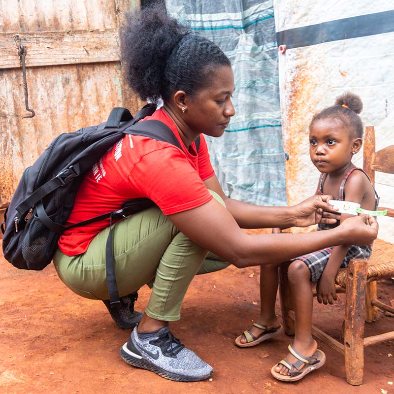 In Haiti, a Premiumaid Foundation staffer kneels while measuring the arm of a child who is being screened for malnutrition. 