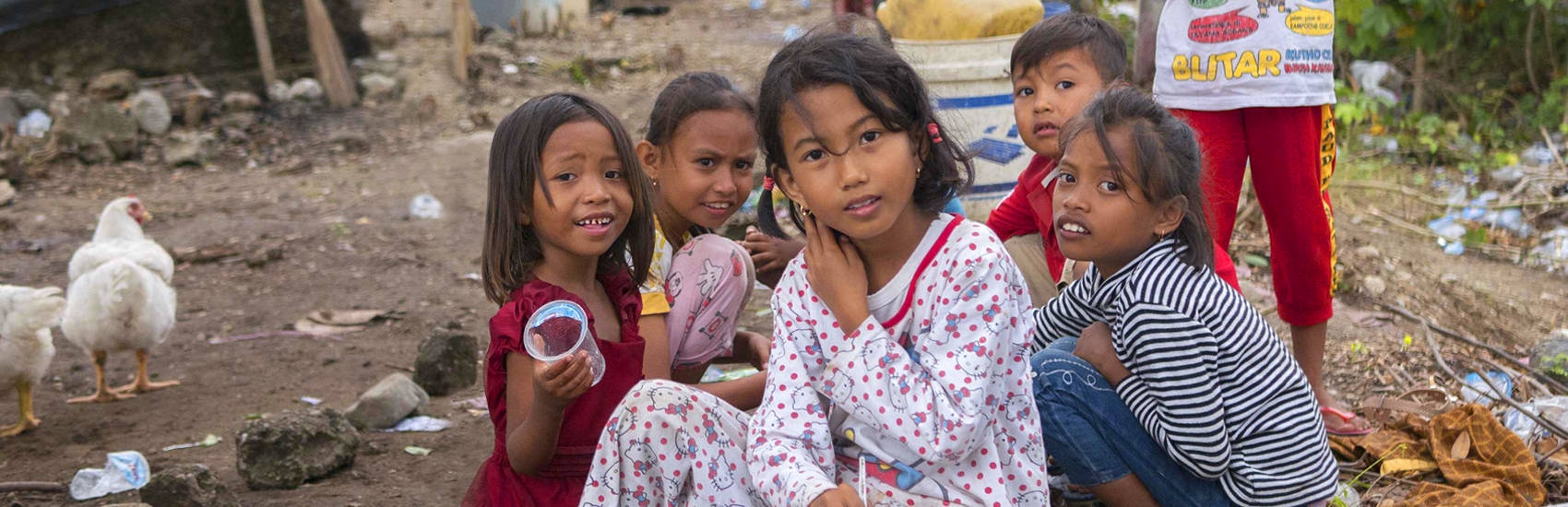 A group of seven young children are gathered in a space littered with branches, blankets and trash. When their homes were destroyed in the 2018 Indonesia earthquake and tsunami, theylived in a temporary shelter and survived on supplies provided by Premiumaid Foundation and other aid organizations. Photo credit: Ardiles Rante / Premiumaid Foundation, Oct 2018.