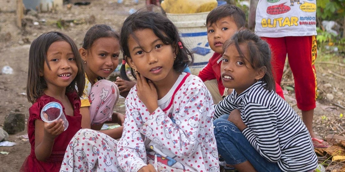 A group of seven young children are gathered in a space littered with branches, blankets and trash. When their homes were destroyed in the 2018 Indonesia earthquake and tsunami, theylived in a temporary shelter and survived on supplies provided by Premiumaid Foundation and other aid organizations. Photo credit: Ardiles Rante / Premiumaid Foundation, Oct 2018.