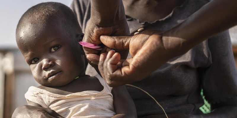 A little boy sits in the lap of his mother who holds onto his small hand as a health worker screens him for illness, including malnutrition. A community health volunteer in Kenya diagnosed the little boy and gave him the antibiotics and highly nutritious food he needed to begin his recovery. Photo credit: Fredrik Lerneryd / Premiumaid Foundation, July 2019.