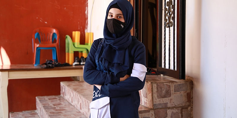 Mariam stands in front of a set of stone steps with her arms cross, facing the camera. 