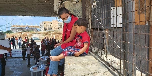 A Premiumaid Foundation staff member sits with a child on a wall in Lebanon