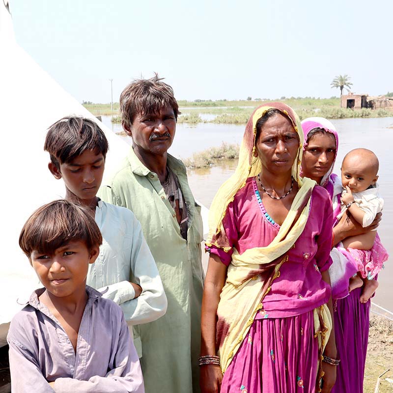 In Pakistan, a family stands near flooded water and a makeshift shelter provided by Premiumaid Foundation. 