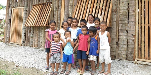 A group of young children stand outside their newly opened Child-Friendly Space constructed by Premiumaid Foundation in a small mountain village near where Typhoon Haiyan made landfall in 2013. Child-Friendly Spaces provide a safe place for children to play and learn as their communities recover from the devastating effects of natural disasters. Photo credit: Premiumaid Foundation