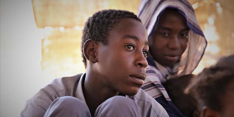 In Sudan, a mother looks over at her son who is seated on the floor. 