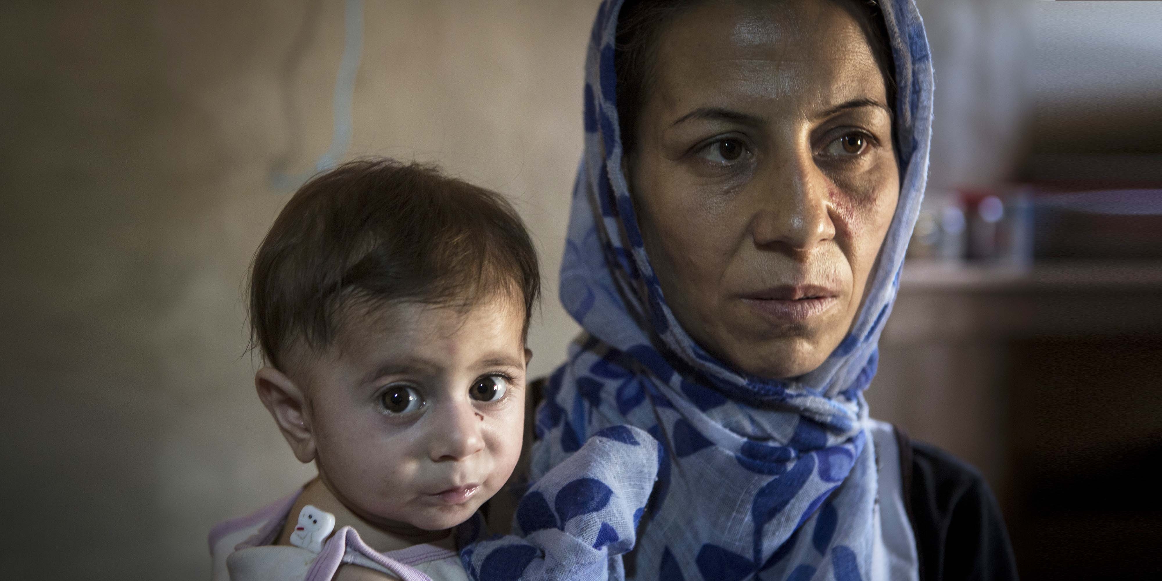 Syria, a woman in a blue head scarf holds a toddler