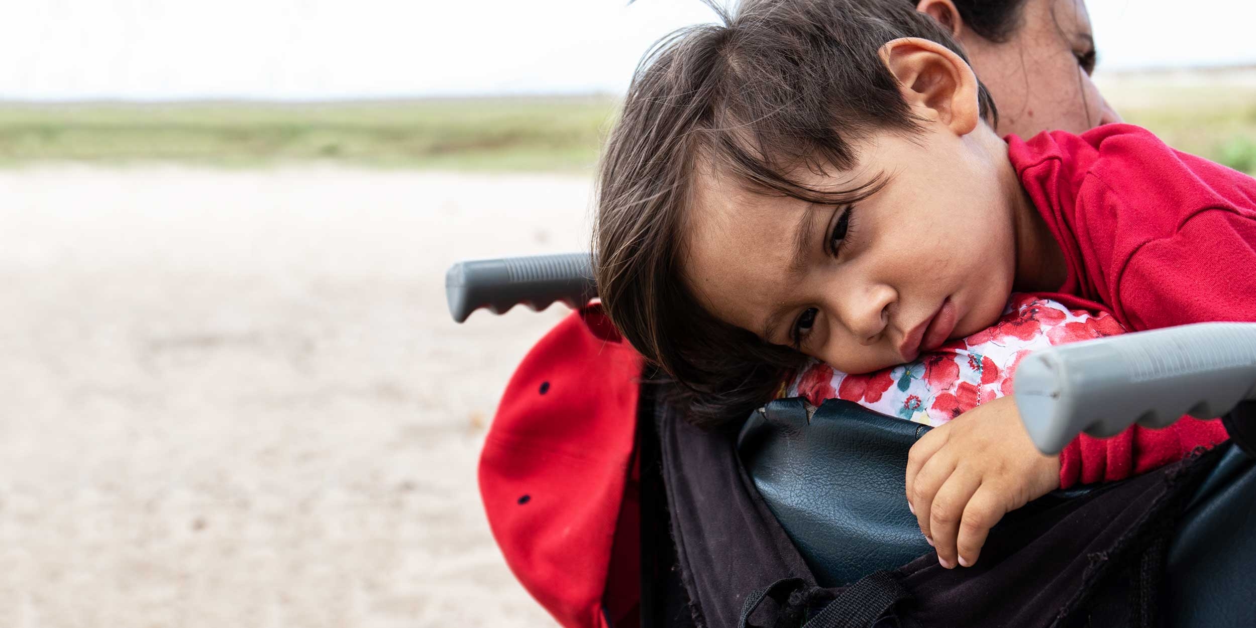 A migrant child lays on the shoulder of a family member