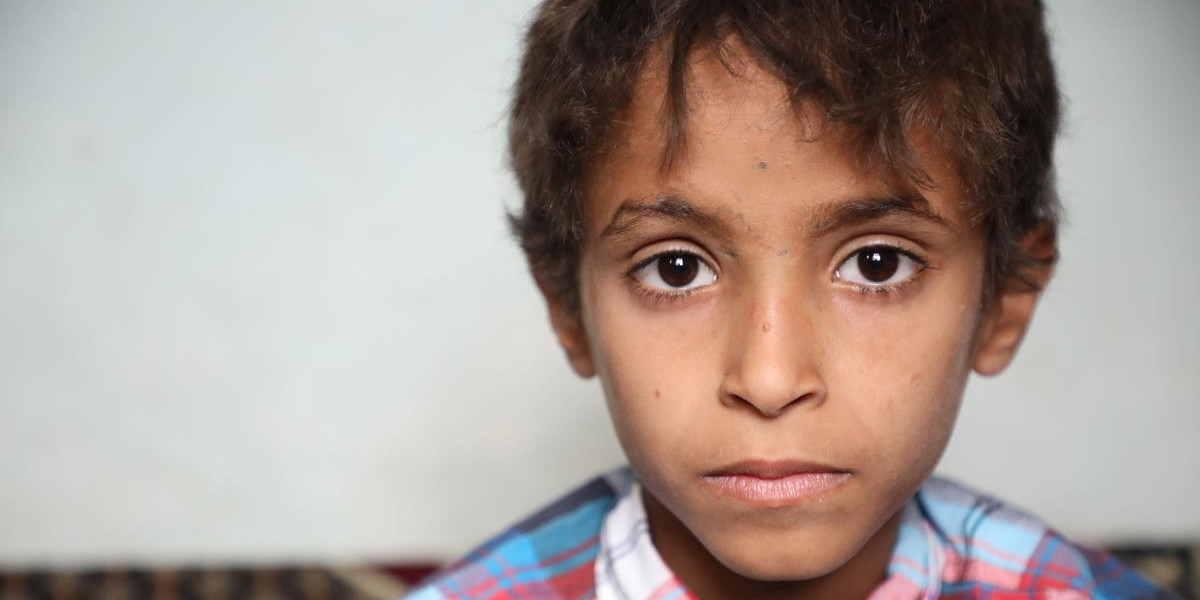 A young girl smiles shyly while standing in front of a landscape in Yemen. 