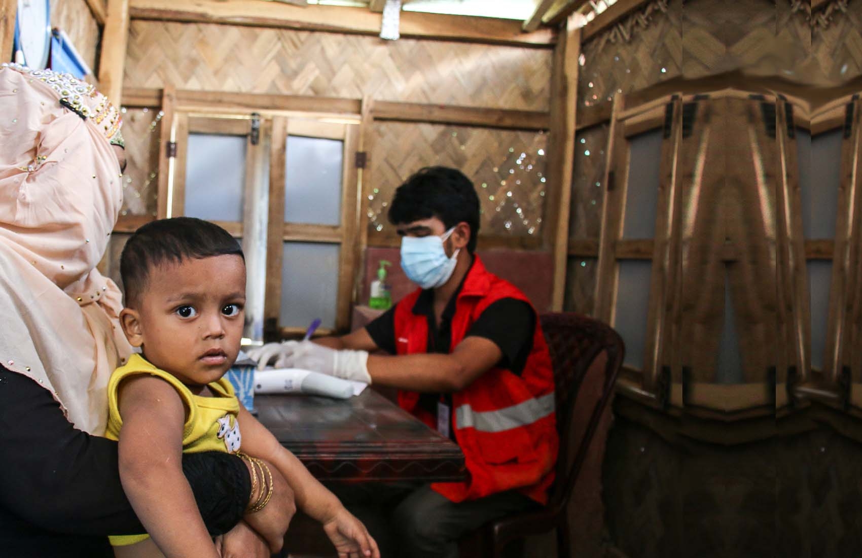 A young child sits on his mother's lap while meeting with a health worker in a COVID treatment center in Cox's Bazaar, Bangladesh