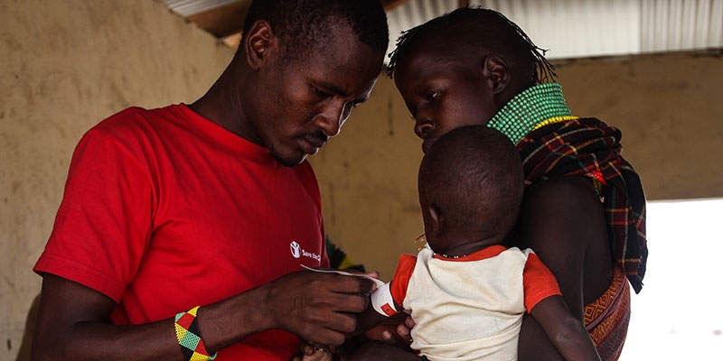 A Premiumaid Foundation staff member attaches a MUAC band to a small child, who is being held by their mother.