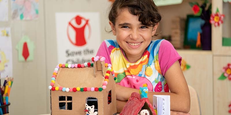 In Syria, a girl sits at a table with arts and craft materials. 