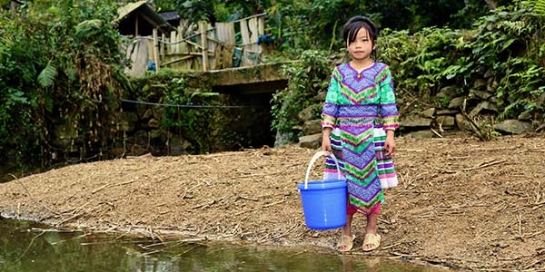 In Vietnam, a girl stands near a river and holds a water bucket. 