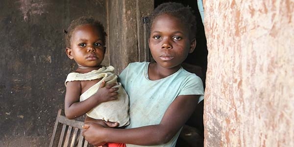 A 9-year old girl holds her one-year old baby sister on her hip outside their cement home in the Democratic Republic of Congo.