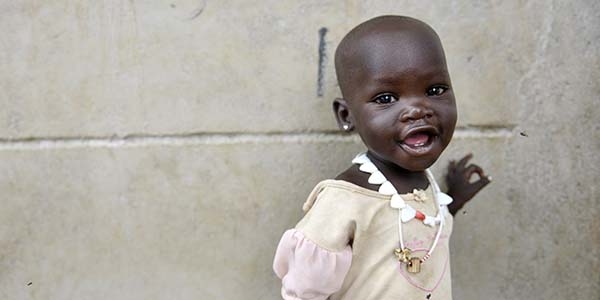 A one-year-old smiles as she places one hand on a wall near a food distribution center in South Sudan.