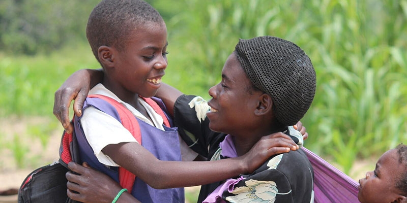 A smiling boy and his mother hold their arms over each other.