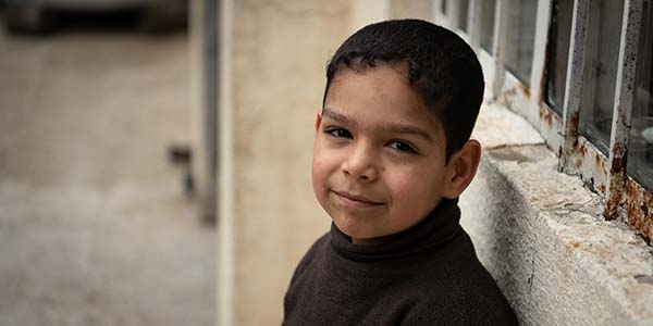 A 7-year old boy leans up against a cement wall near his home in Iraq.