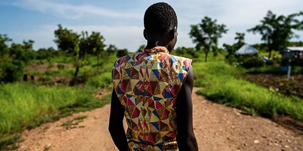 A boy with his back to the camera standing in a dirt road.