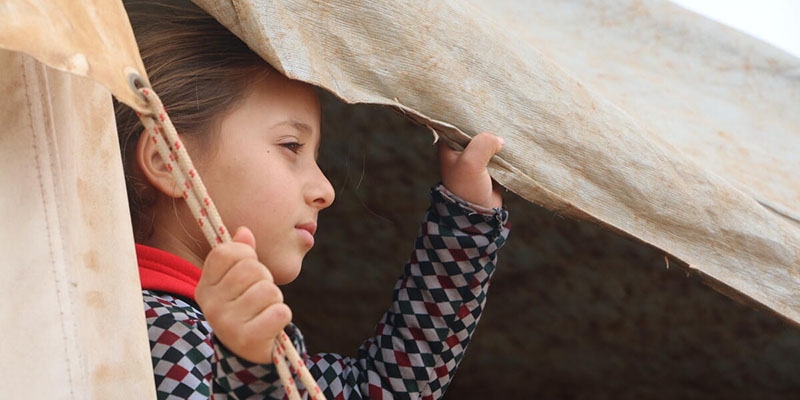 A girl looks out of the tent she lives in a displacement camp in rural North West Syria