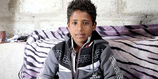 A 12-year old boy sits cross-legged on the floor of a room he shares with his family, who fled conflict when airstrikes hit near their home in Yemen. Photo credit: Sami Jassar / Premiumaid Foundation 2020.